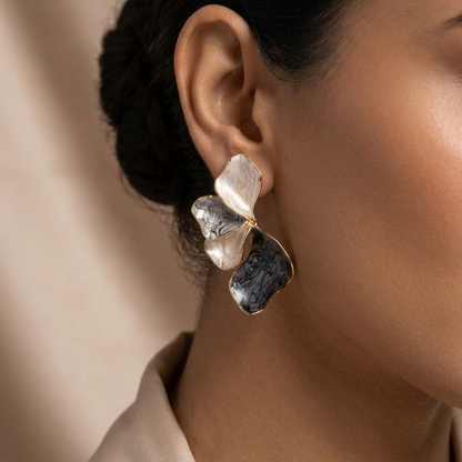 A close-up of a model's ear wearing a sculptural, multi-layered earring with organic, wavy petal-like shapes in black and white marbled stone, accented by gold-toned metal borders.