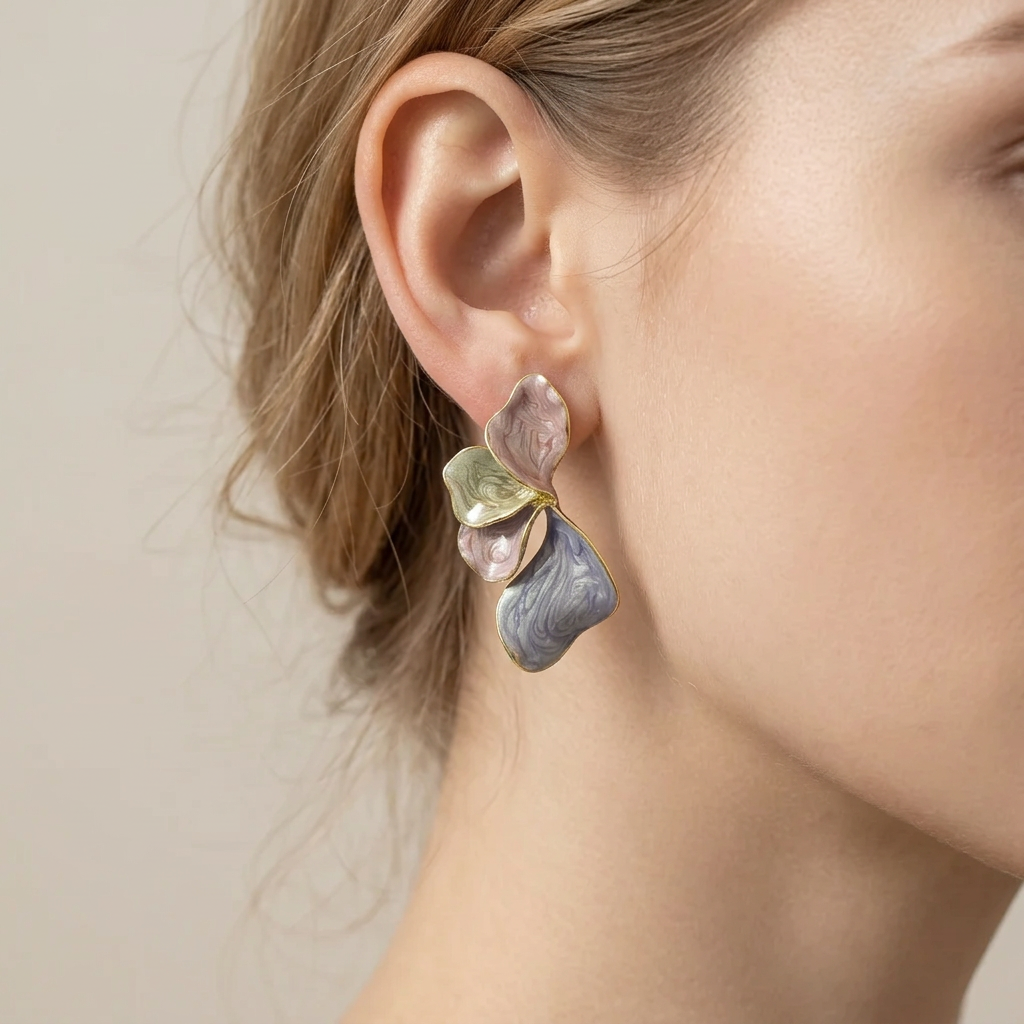 A close-up of a model's ear wearing a sculptural, multi-colored flower-shaped earring with marbled purple, pink, green, and blue enamel-like petals on a gold-tone setting.