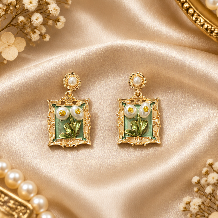 A pair of vintage-style floral drop earrings with gold-tone frames, green enamel, white flower faces, and pearl-like centers.